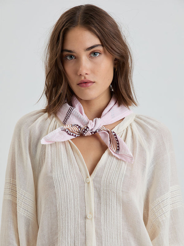 Woman wearing a light pink scarf with a pattern around her neck against a white background