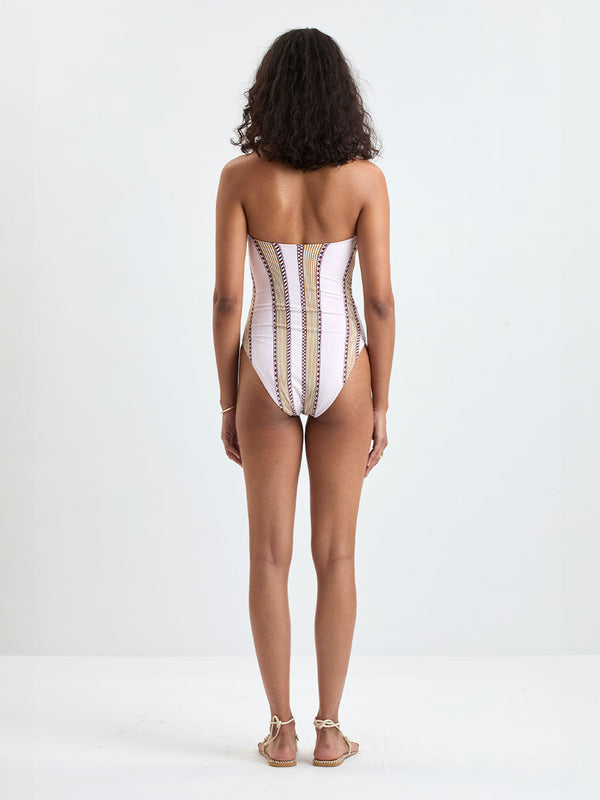 back of a Woman Standing wearing lemlem DINHA One Piece featuring detailed bands of deep burgundy, bronze, and pink stripes beautifully placed on a light cream 