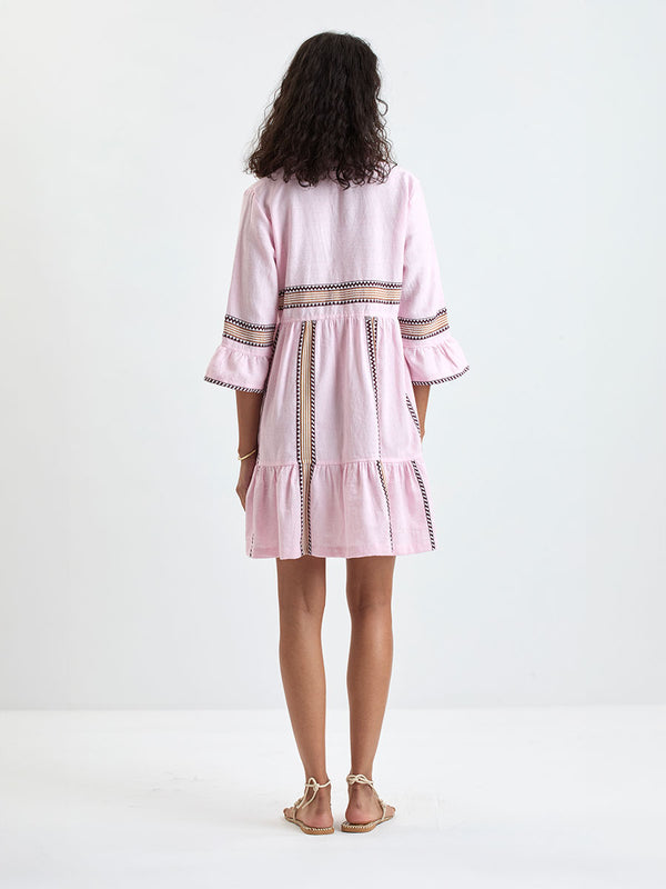 Woman Standing wearing lemlem HANNA Dress featuring detailed bands of deep burgundy, bronze, and pink stripes beautifully placed on a light cream 
