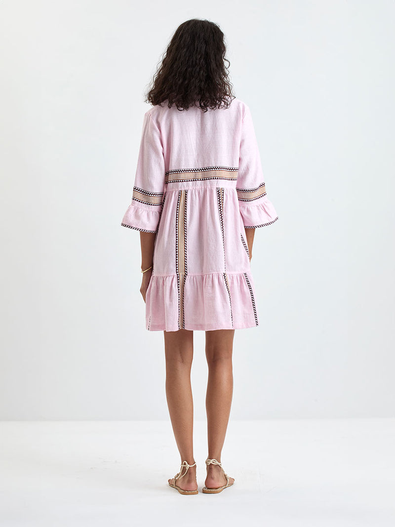Woman Standing wearing lemlem HANNA Dress featuring detailed bands of deep burgundy, bronze, and pink stripes beautifully placed on a light cream 