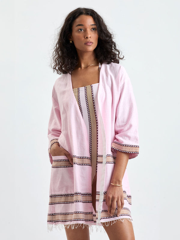 Woman Standing wearing lemlem handwoven IMANI Robe and DINHA One Piece featuring detailed bands of deep burgundy, bronze, and pink stripes beautifully placed on a light cream 