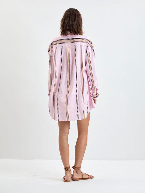 back of a Woman Standing wearing lemlem MARIAM Shirt featuring detailed bands of deep burgundy, bronze, and pink stripes beautifully placed on a light cream 