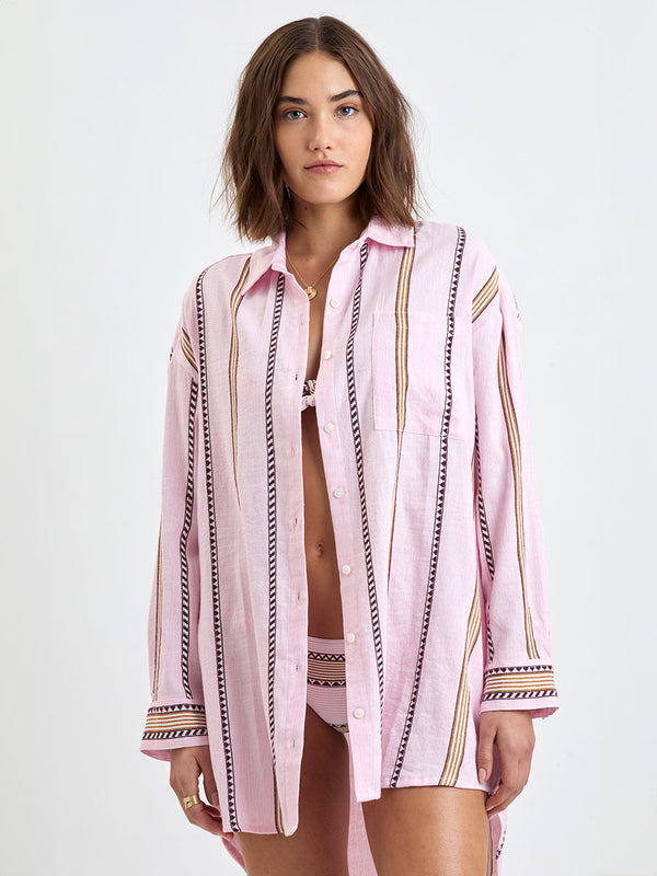 Woman Standing wearing lemlem MARIAM Shirt featuring detailed bands of deep burgundy, bronze, and pink stripes beautifully placed on a light cream 