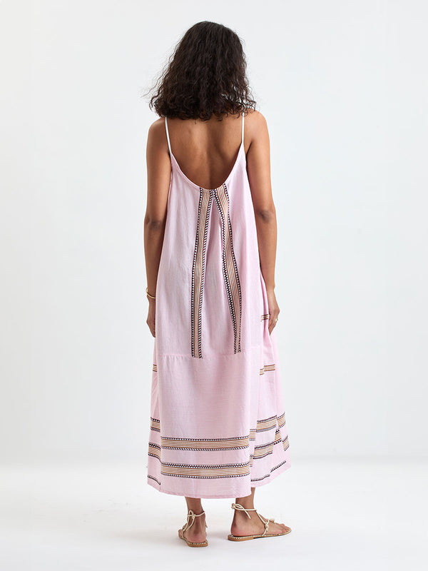 Back of a Woman Standing wearing lemlem NIA Slip Dress featuring detailed bands of deep burgundy, bronze, and pink stripes beautifully placed on a light cream 