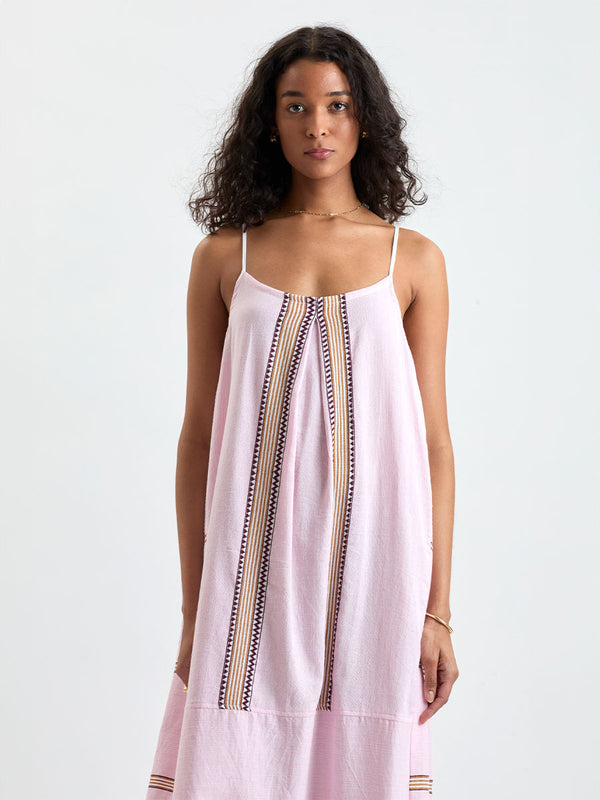 Woman Standing wearing lemlem handwoven NIA Slip Dress featuring detailed bands of deep burgundy, bronze, and pink stripes beautifully placed on a light cream 
