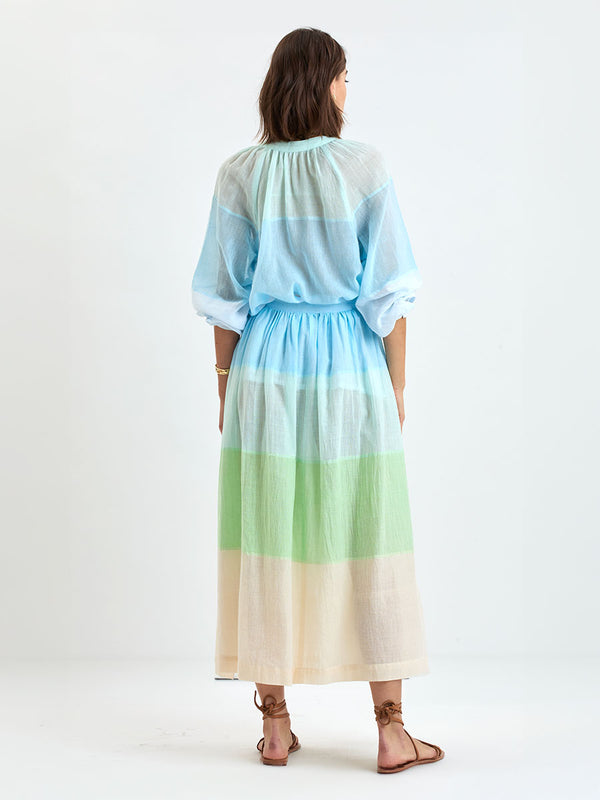 Back of a Woman Standing Wearing handwoven lemlem skirt featuring light, gauzy fabric with a beautiful color block of light blue, aqua, mint, soft green and cream colors and matching blouse