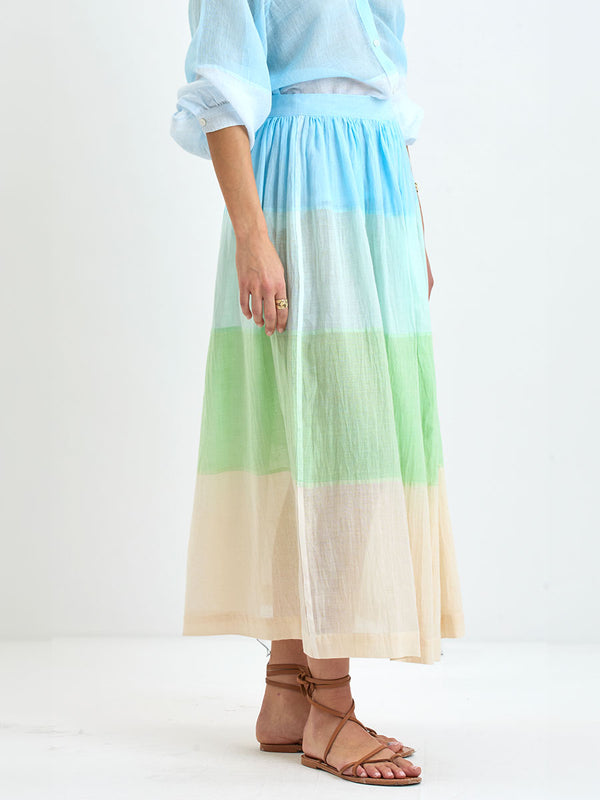 Close up on a Woman Standing Wearing handwoven lemlem skirt featuring light, gauzy fabric with a beautiful color block of light blue, aqua, mint, soft green and cream colors and matching blouse