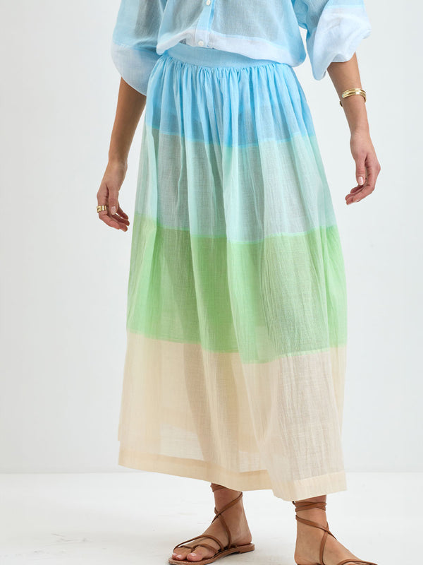Close up on a Woman Standing Wearing handwoven lemlem skirt featuring light, gauzy fabric with a beautiful color block of light blue, aqua, mint, soft green and cream colors and matching blouse