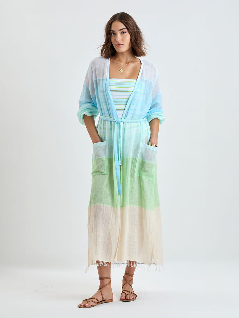 Woman wearing lemlem handwoven MATARA Robe featuring light, gauzy fabric with a beautiful color block of light blue, aqua, mint, soft green and cream
