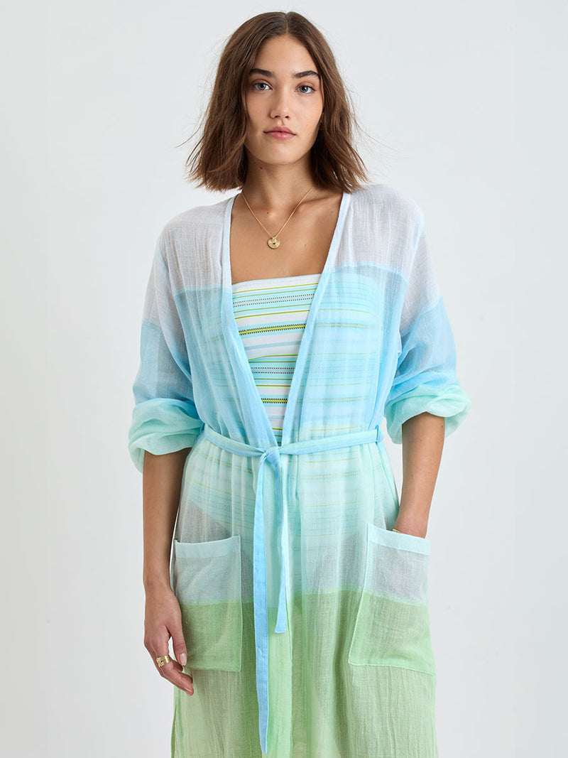 Woman wearing lemlem handwoven MATARA Robe featuring light, gauzy fabric with a beautiful color block of light blue, aqua, mint, soft green and cream