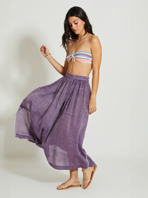 Side shot of a Woman Standing Wearing lemlem FREYE | Skirt featuring sheer fabric in rich plum color