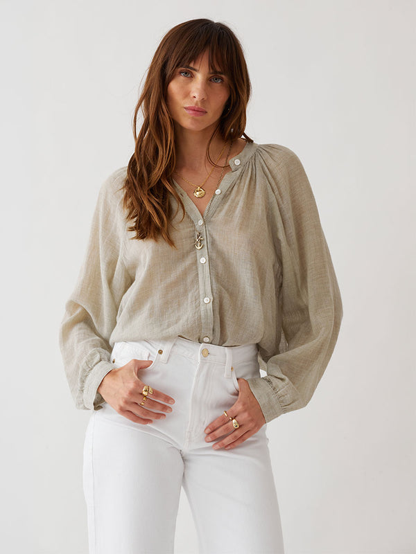 Woman standing wearing lemlem MITA Blouse featuring sheer handwoven fabric in sage color