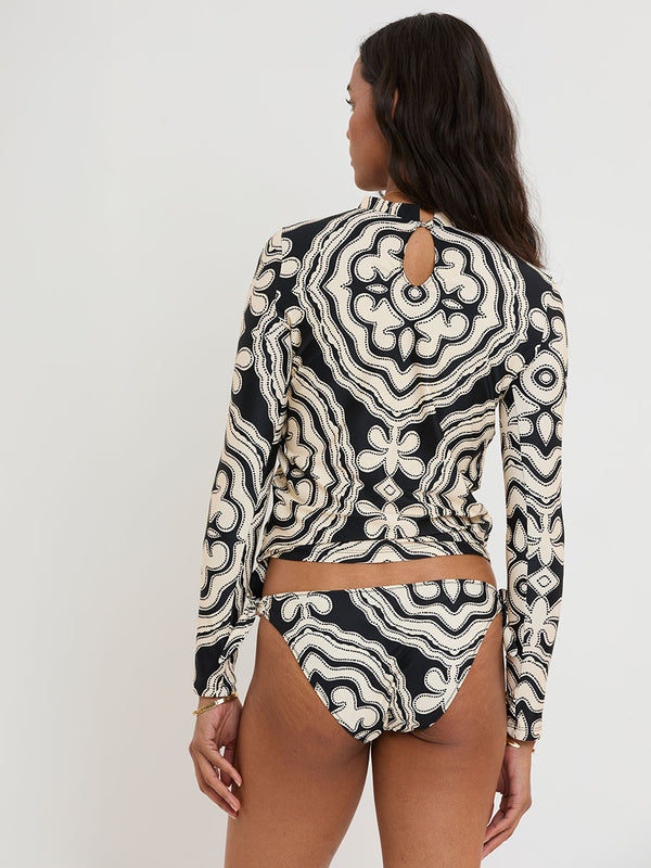 Back of a Woman standing wearing lemlem AZEB Rash Guard and LUCY Side Tie Bottom featuring ancient inspired pattern in creamy ivory perfectly grounded by rich black for a striking and timeless look.