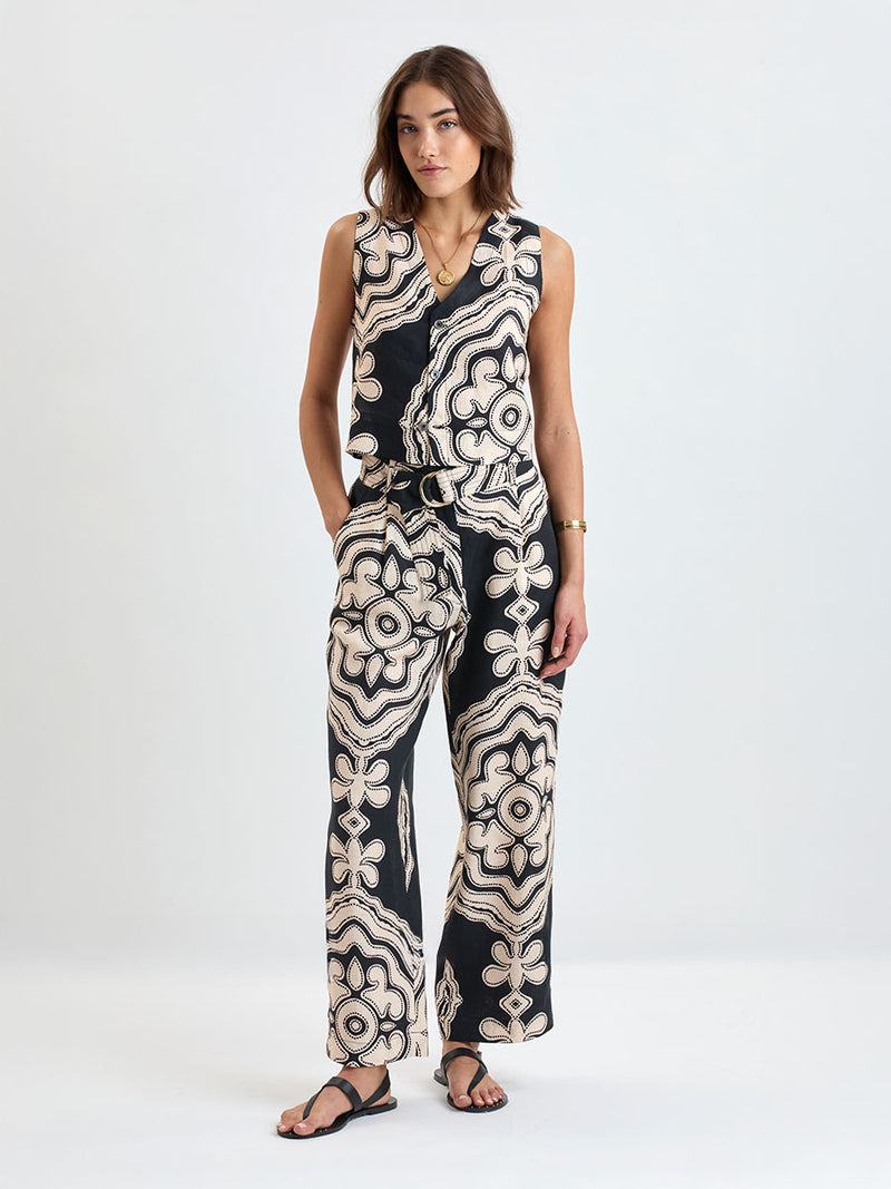 Woman standing wearing lemlem DIRARRA Pants featuring ancient inspired pattern in cream color on black background and a matching tank top
