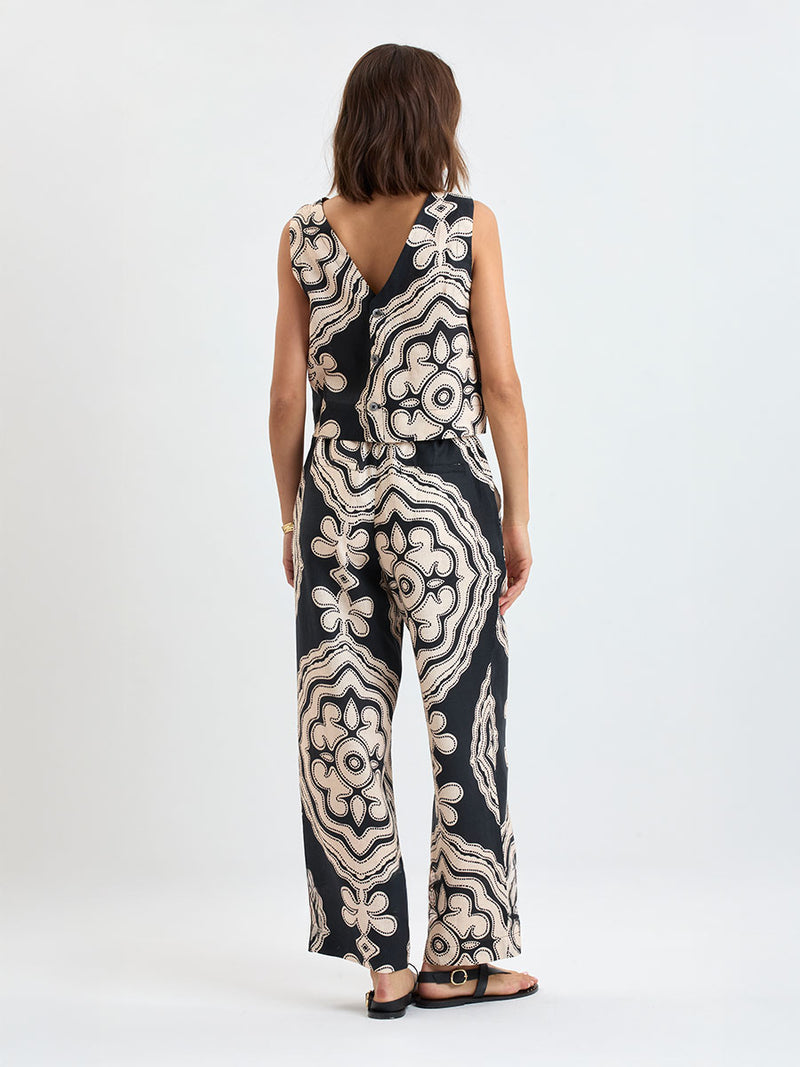 Back of a woman standing wearing lemlem DIRARRA Pants featuring ancient inspired pattern in cream color on black background and a matching tank top