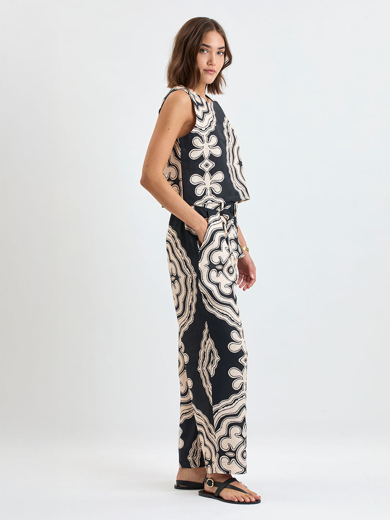 Woman standing wearing lemlem DIRARRA Pants featuring ancient inspired pattern in cream color on black background and a matching tank top