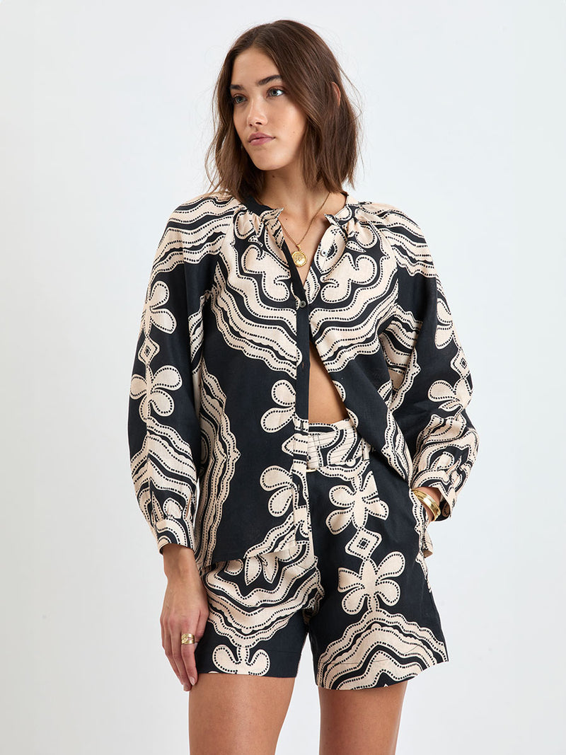 Woman wearing lemlem linen  FAIZAH Shorts featuring  a custom-designed print inspired by ancient architectural patterns in cream and black colors and a matching shorts