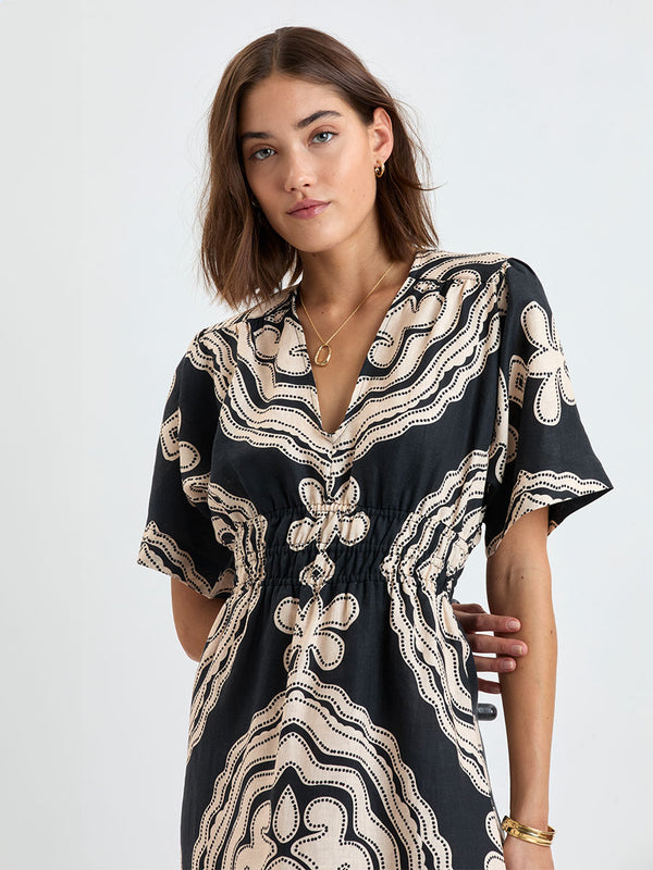 Close up on a  Woman Standing wearing lemlem linen HERMONA Plunge Dress  featuring  a custom-designed print inspired by ancient architectural patterns in cream and black colors