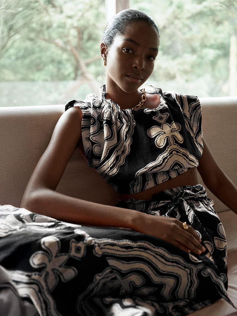 Woman sitting wearing lemlem cropped top and long skirt featuring cream pattern on black background