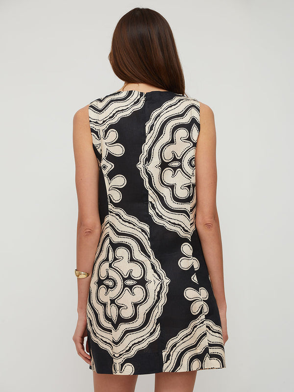 Woman standing wearing lemlem PERSINNA linen dress featuring ancient inspired pattern in cream color on black background