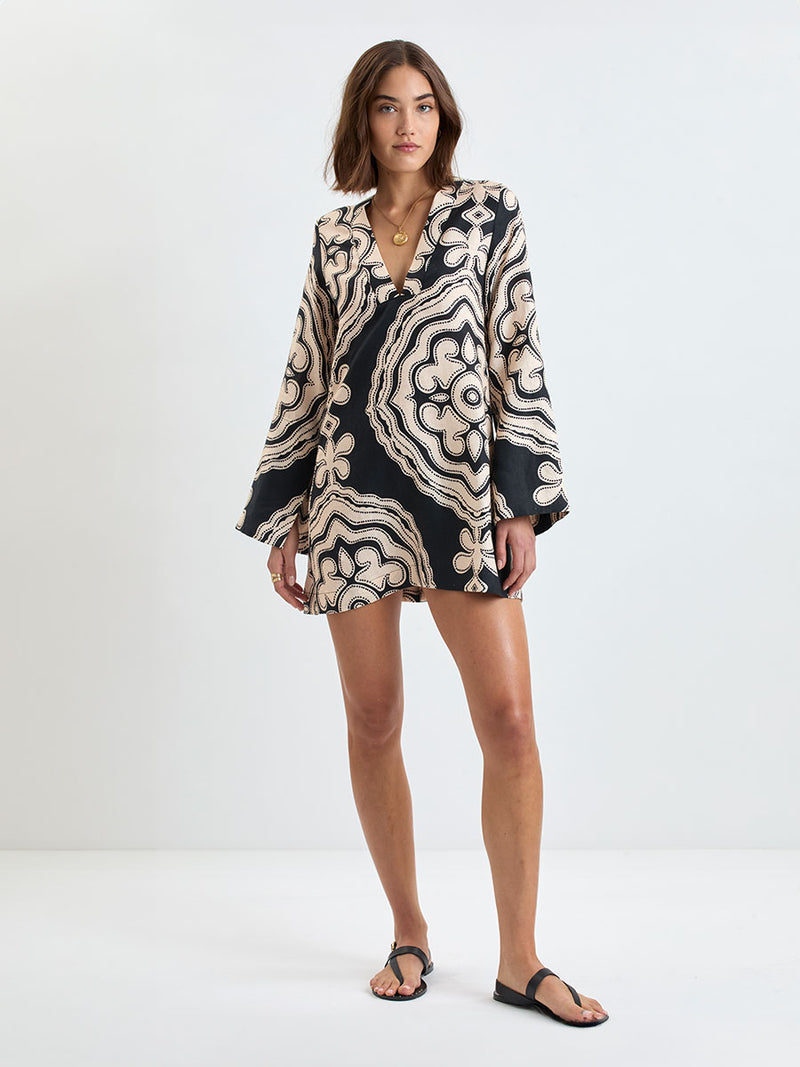 Woman Standing wearing lemlem linen RAEY Column Dress  featuring  a custom-designed print inspired by ancient architectural patterns in cream and black colors