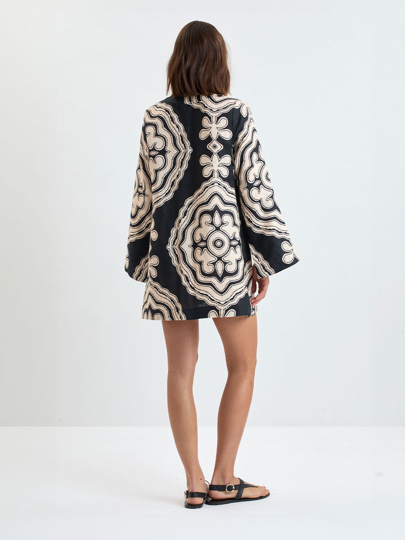 Back of a Woman Standing wearing lemlem linen RAEY Column Dress  featuring  a custom-designed print inspired by ancient architectural patterns in cream and black colors