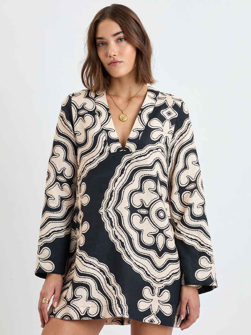 Woman Standing wearing lemlem linen RAEY Column Dress  featuring  a custom-designed print inspired by ancient architectural patterns in cream and black colors