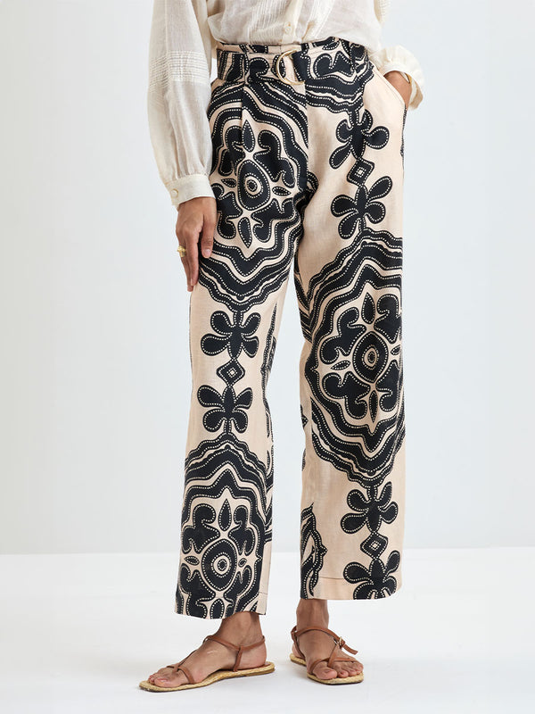 Close up on a Woman Standing wearing lemlem MITA Blouse in cream color and DIARRA Pants featuring ancient inspired pattern in black color on cream background and beige denim shorts