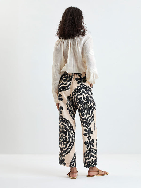Back of a Woman Standing wearing lemlem MITA Blouse in cream color and DIARRA Pants featuring ancient inspired pattern in black color on cream background