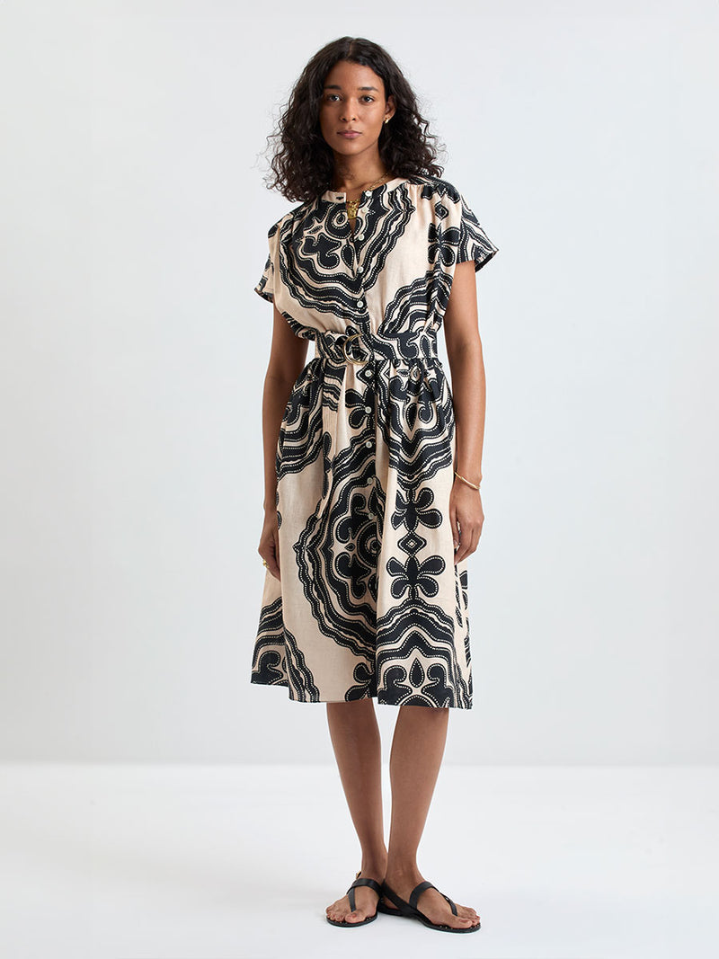 Woman Standing wearing lemlem HERAT Dress featuring ancient inspired pattern in black color on cream background