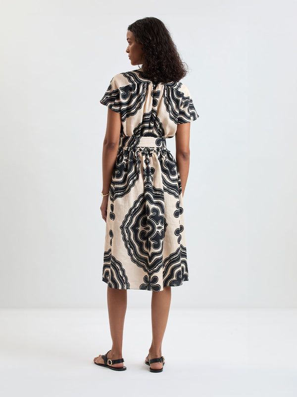 Back of a Woman Standing wearing lemlem HERAT Dress featuring ancient inspired pattern in black color on cream background
