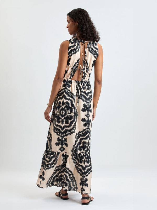 Back of a Woman Standing wearing lemlem LELISA Dress featuring ancient inspired pattern in black color on cream background and beige denim shorts