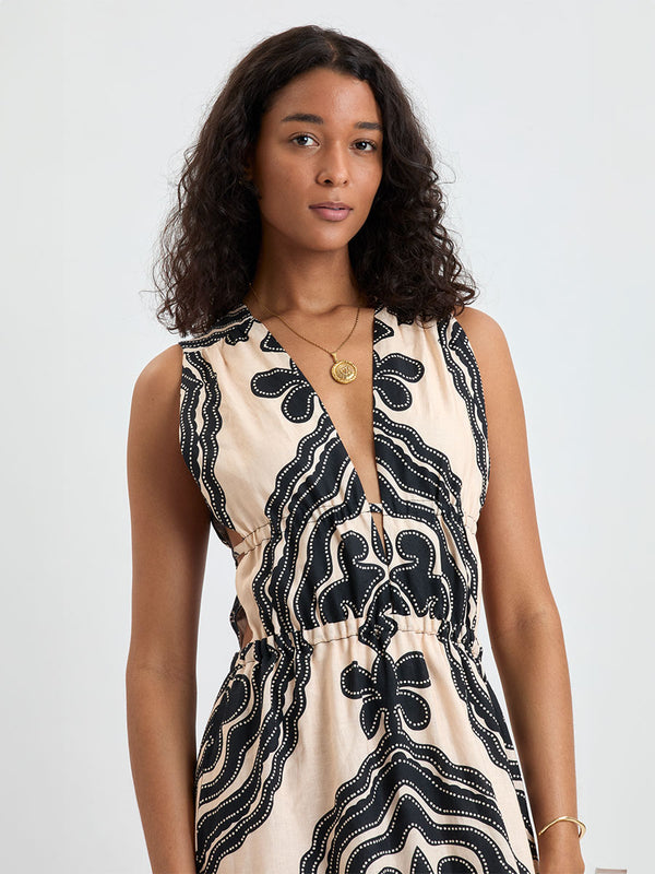 Woman Standing wearing lemlem LELISA Dress featuring ancient inspired pattern in black color on cream background and beige denim shorts