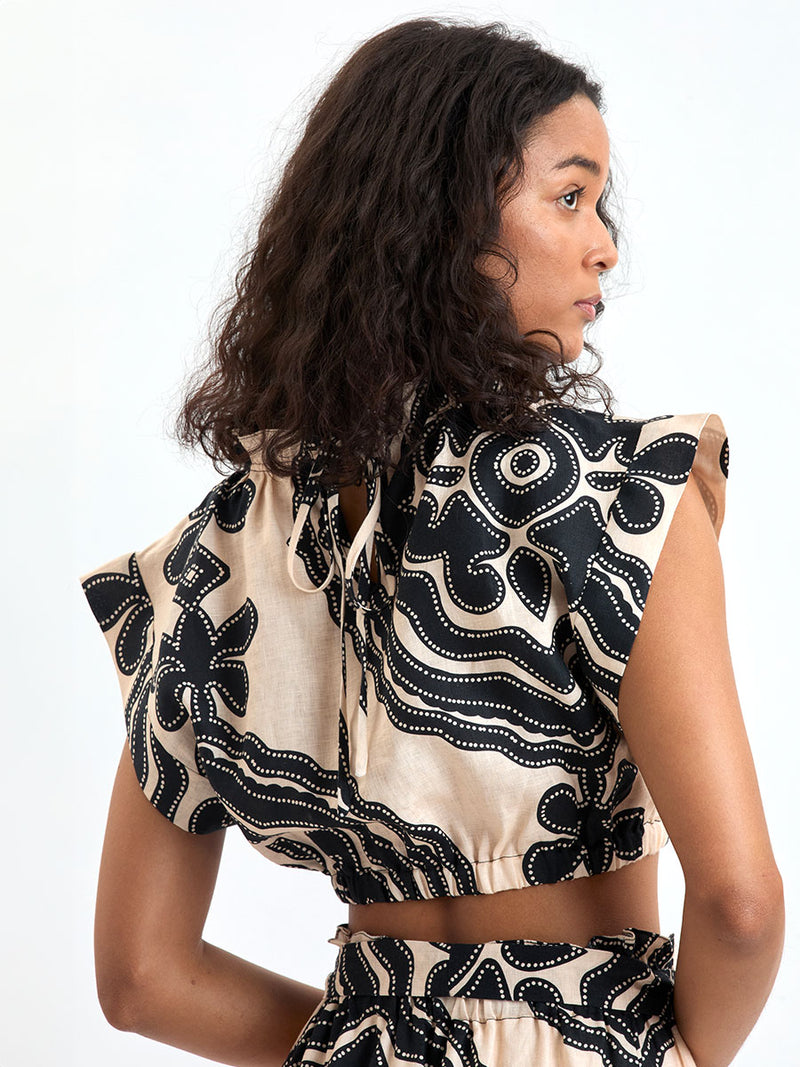 Back of a Woman Standing wearing lemlem MUNA Top and SANAA Skirt featuring ancient inspired pattern in black color on cream background and beige denim shorts