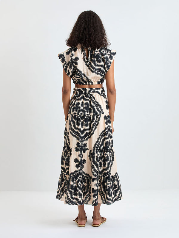 Back of a Woman Standing wearing lemlem MUNA Top and SANAA Skirt featuring ancient inspired pattern in black color on cream background and beige denim shorts