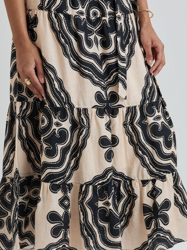 Woman Standing wearing lemlem SANAA Skirt featuring ancient inspired pattern in black color on cream background and beige denim shorts