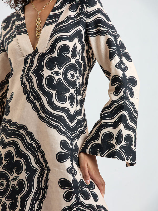 Woman Standing wearing lemlem THEODORA Dress featuring ancient inspired pattern in black color on cream background and beige denim shorts