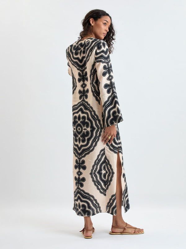 Back of a Woman Standing wearing lemlem THEODORA Dress featuring ancient inspired pattern in black color on cream background and beige denim shorts