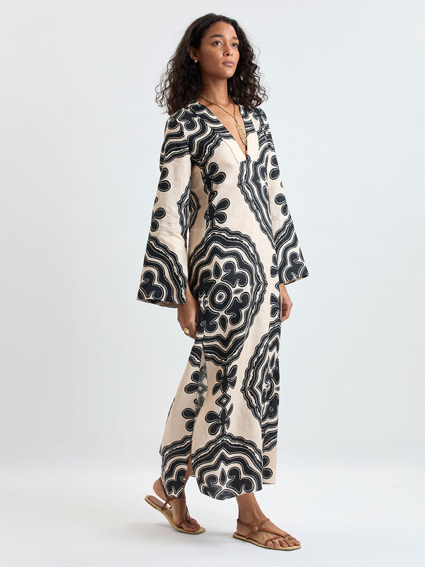 Back of a Woman Standing wearing lemlem THEODORA Dress featuring ancient inspired pattern in black color on cream background and beige denim shorts