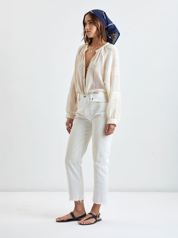 Woman standing wearing lemlem handwoven DANA Bandana featuring white tibeb pattern on navy background and handwoven MITA Blouse featuring cream color