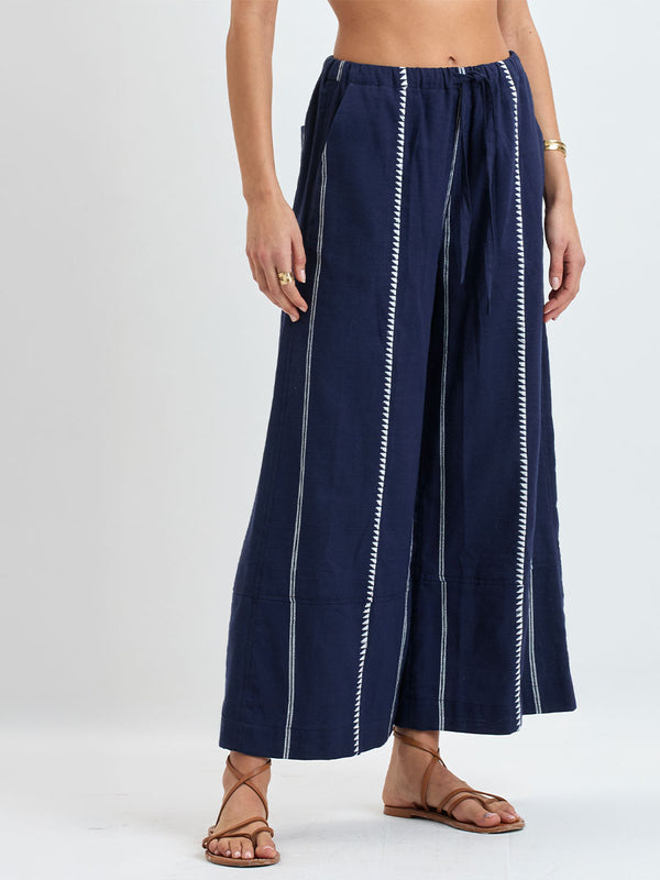 Close up on a Woman standing wearing lemlem handwoven DESTA Pants featuring white tibeb pattern on navy background 