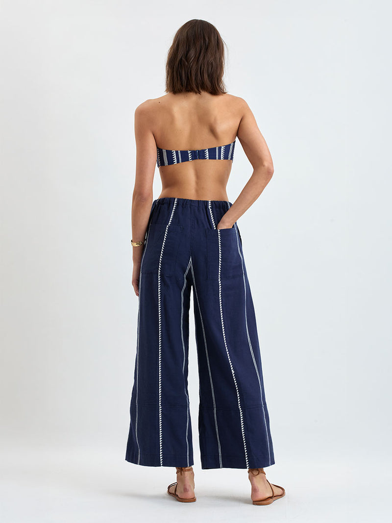 Back of a Woman standing wearing lemlem handwoven DESTA Pants featuring white tibeb pattern on navy background 