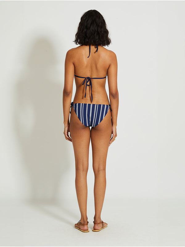 Back of a woman standing with her arms over her head  wearing a navy Nunu triangle top with white triangles and stripes and matching string bikini bottom
