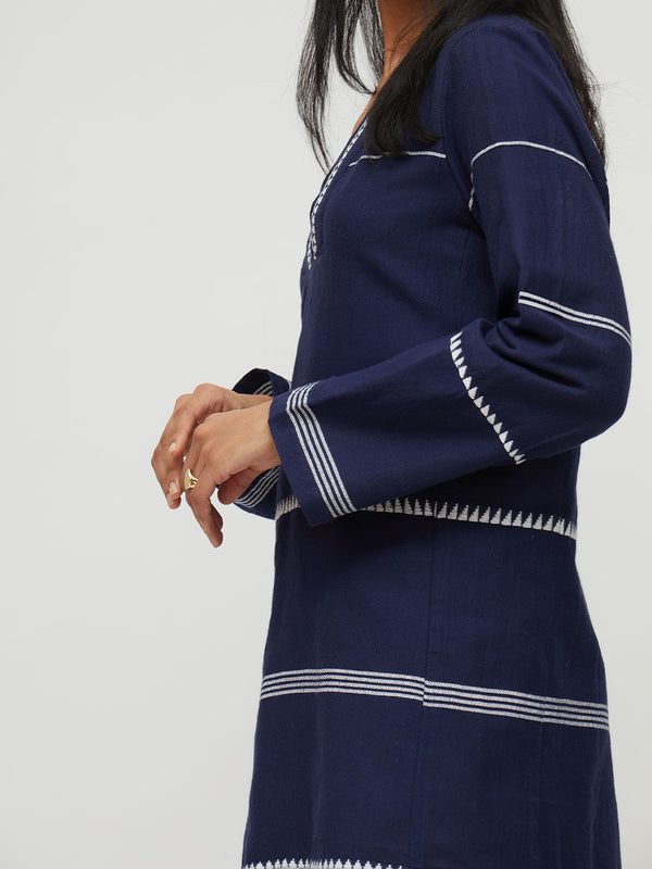A navy blue long-sleeve lemlem handwoven dress with white geometric embroidered trim, shown on a model against a light gray background.
