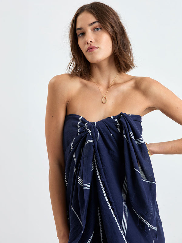 Woman standing wearing lemlem handwoven TALAKI Sarong featuring delicate white Tibeb bands on a rich navy silhouette