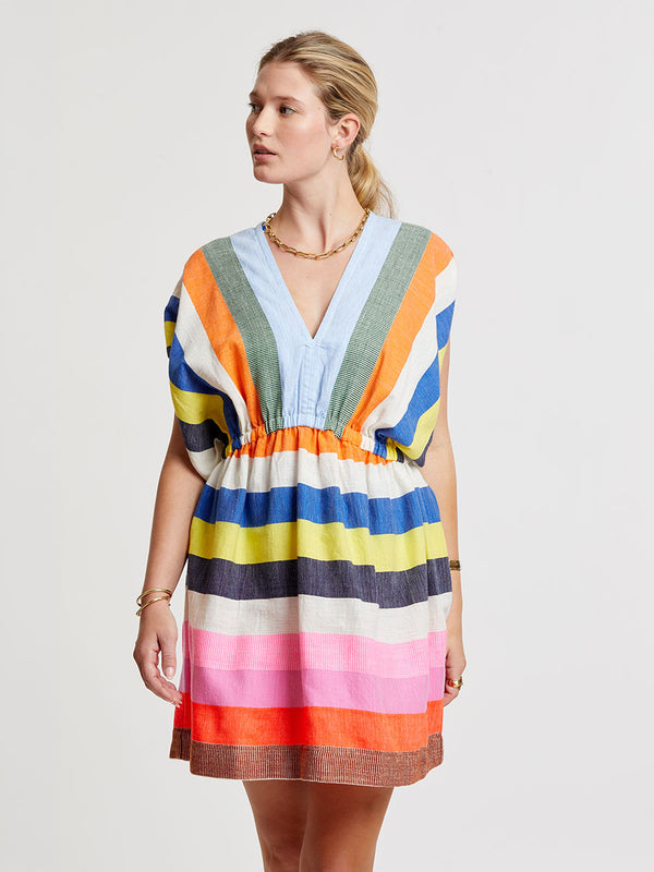 Woman wearing lemlem handwoven ALEM Plunge Dress featuring bold, joyful stripe pattern in vibrant shades of blue, yellow, pink, orange, and green