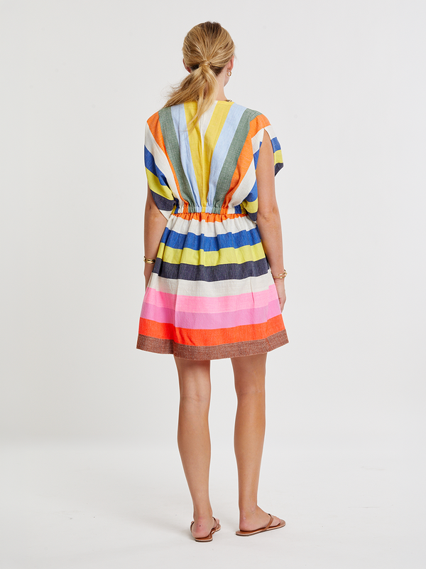 Woman wearing lemlem handwoven ALEM Plunge Dress featuring bold, joyful stripe pattern in vibrant shades of blue, yellow, pink, orange, and green