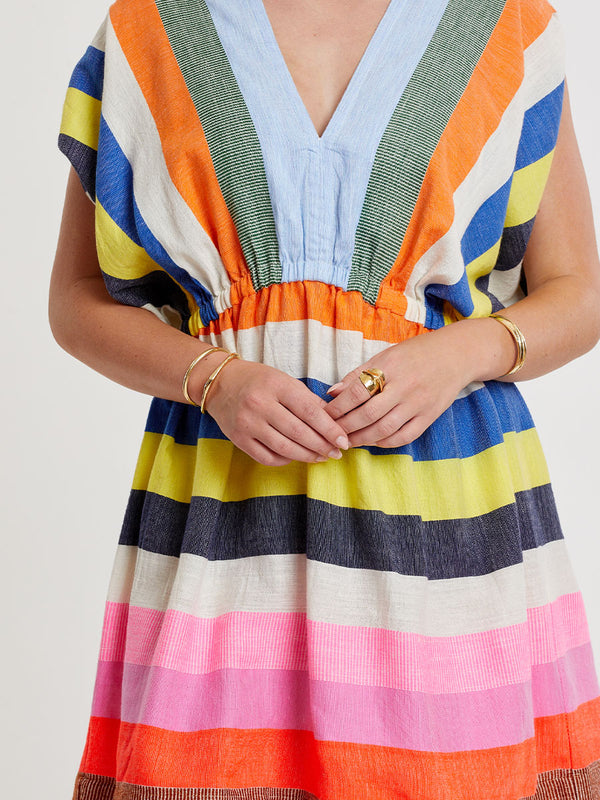 Woman wearing lemlem handwoven ALEM Plunge Dress featuring bold, joyful stripe pattern in vibrant shades of blue, yellow, pink, orange, and green