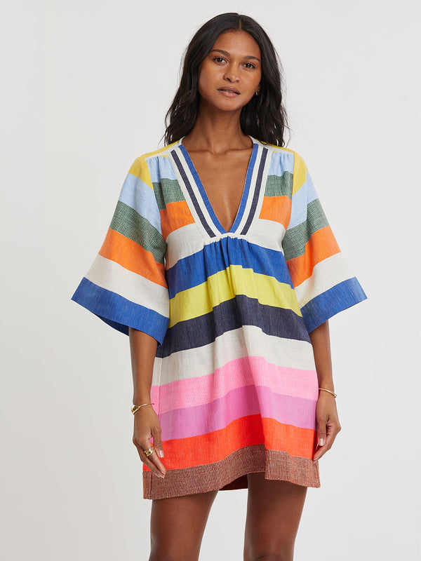 Woman wearing lemlem handwoven BELKIS Dress featuring bold, joyful stripe pattern in vibrant shades of blue, yellow, pink, orange, and green