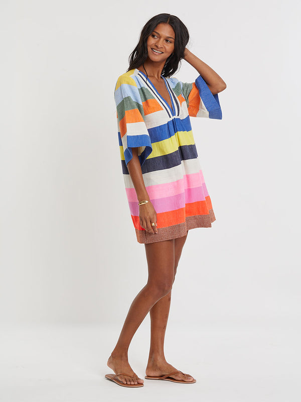 Woman wearing lemlem handwoven BELKIS Dress featuring bold, joyful stripe pattern in vibrant shades of blue, yellow, pink, orange, and green